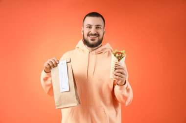 Lezzetli sandviç dürümü ve turuncu arka planda kese kağıdı olan genç adam.