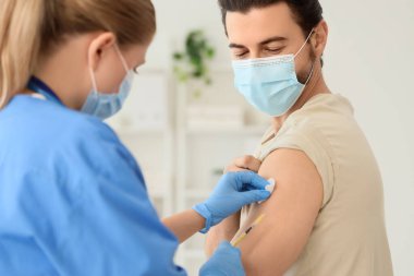 Tıbbi maskeli genç adam klinikteki doktordan aşı alıyor.