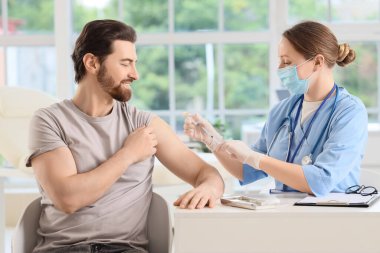 Genç adam klinikteki doktordan aşı alıyor.