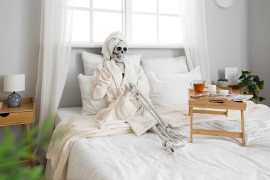 Yatak odasında bornozu ve tepsisi olan insan iskeleti modeli.