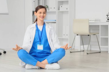 Kadın doktor klinikte yerde meditasyon yapıyor.