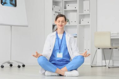 Kadın doktor klinikte yerde meditasyon yapıyor.