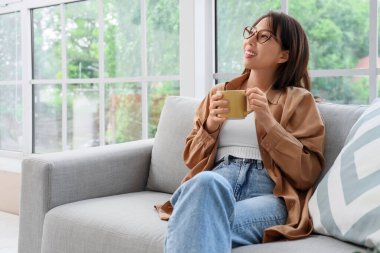 Evdeki kanepede oturan bir fincan kahveli genç Asyalı kadın.