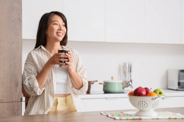 Mutfaktaki masada bir fincan kahveli genç Asyalı kadın.