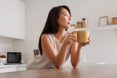 Mutfaktaki masada bir fincan kahveli genç Asyalı kadın.