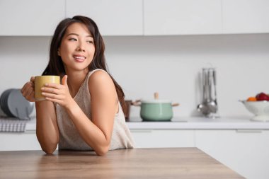 Mutfaktaki masada bir fincan kahveli genç Asyalı kadın.