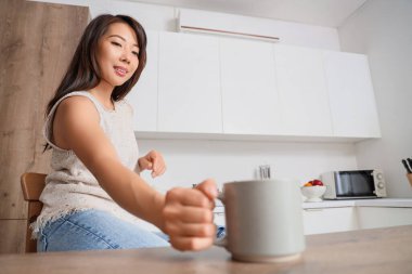 Mutfaktaki masada bir fincan kahveli genç Asyalı kadın.