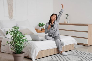 Yatak odasında uzanan bir fincan kahveli genç Asyalı kadın.