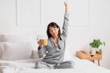 Yatak odasında uzanan bir fincan kahveli genç Asyalı kadın.