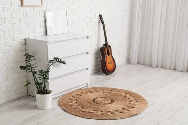Odada gitar, bitki ve hasır kaplı çekmeceler var.