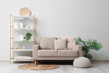 Oturma odasının içinde kanepe, raf ünitesi ve hasır halı var.