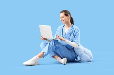 Mavi arka planda dizüstü bilgisayarla çalışan kadın stajyer.