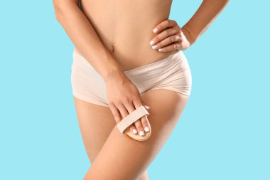 İç çamaşırlı genç bir kadın selülit sorunu yaşıyor. Mavi arka planda bacağına masaj yapıyor. Yakın plan.