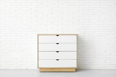 Odanın hafif tuğlalı duvarının yanındaki beyaz çekmeceler.