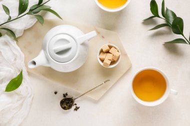 Bir fincan çay, çaydanlık ve arka planda kuru yapraklı kaşık.