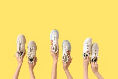 Sarı arka planda farklı spor ayakkabıları olan kadın eller.