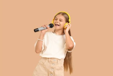 Kulaklıklı, mikrofonlu, bej arka planda şarkı söyleyen küçük kız.