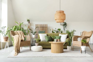 Yeşil kanepesi, koltuğu ve çiçekleri olan aydınlık oturma odasının içinde.