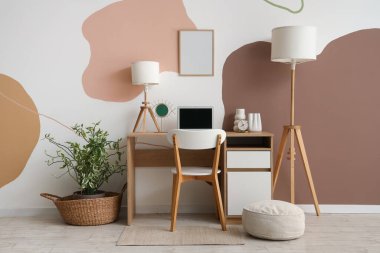 Modern dizüstü bilgisayarı ve beyaz duvarın yanındaki lambası olan şık masa.