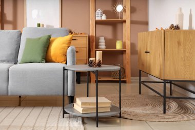 Oturma odasının içinde büyük kitaplar, mumlar ve koniler olan rahat bir kanepe ve kahve masası.