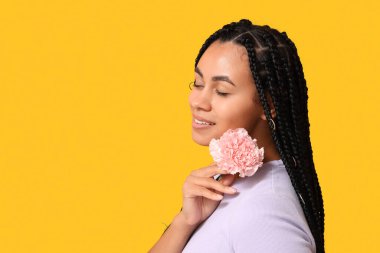 Sarı arka planda karanfil çiçeği olan güzel bir Afro-Amerikalı kadın.