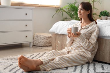 Pijamalı güzel, genç ve mutlu bir kadın. Evde yerde oturmuş çay içiyor.