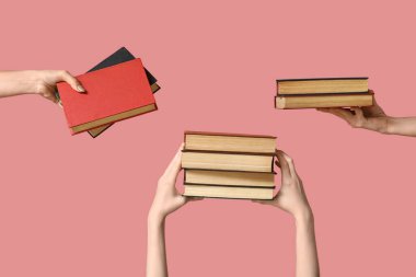 Pembe arka planda bir sürü kitap tutan eller