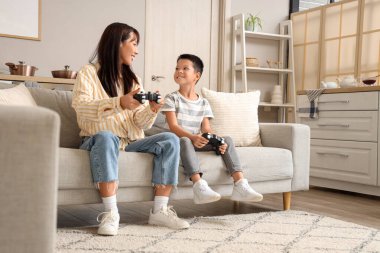 Genç anne ve küçük oğlu evde video oyunu oynuyorlar.