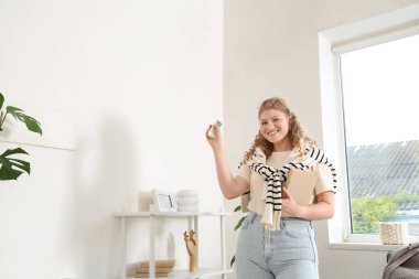 Güzel, gülümseyen bir kadın oturma odasında klimayı açıyor.