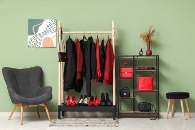 Modern giyinme odasının şık iç dekorasyonu, kadın kıyafetleri ve renkli duvarın yanındaki koltuk.