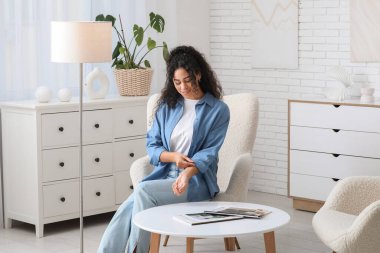 Güzel bir Afro-Amerikalı kadın şık mavi gömleğini ilikliyor ve evdeki koltukta oturuyor.