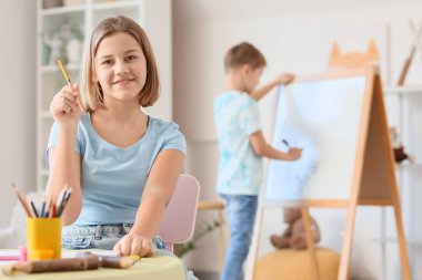 Kalemle masada oturan genç kız.