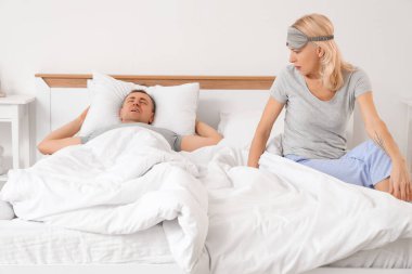 Yatak odasında horlayan kocasıyla sinirli olgun bir kadın.