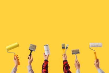 Sarı arkaplanda ressam aletleri olan birçok el