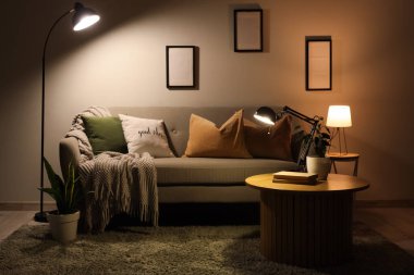 Geceleri karanlık oturma odasının içinde kanepe, masa ve parlayan lambalar var.