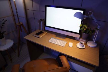 Çalışma odası, boş bilgisayar monitörü ve karanlık ofisteki masasında parlayan lamba.