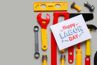 Oyuncak yapım araçları ve gri arkaplanda Mutlu Günler yazılı tebrik kartı. İşçi Bayramı kutlamaları