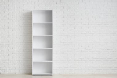 Odadaki beyaz tuğla duvarın yanındaki boş kitaplık.