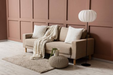 Oturma odasının iç tarafındaki kahverengi duvarın yanında rahat bir kanepe ve puf.