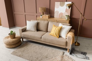 Rahat bir kanepe, puf ve zemin lambası oturma odasının içindeki kahverengi duvarın yanında.