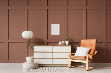 Kahverengi deri koltuk, puf ve göğüs. Oturma odasının iç tarafındaki kahverengi duvarın yanında.