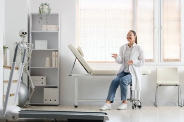 Ofisteki koltukta oturan insan iskeleti modeli olan kadın fizyoterapist.