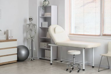 Kanepe, raf ünitesi ve insan iskeleti olan fizyoterapist ofisi.