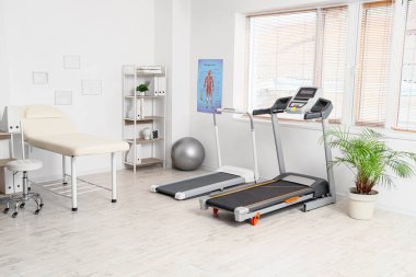 Koltuğu, koşu bandı ve raf ünitesi olan bir fizyoterapist ofisi.