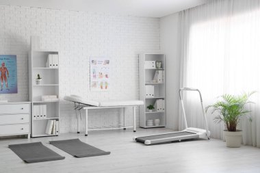 Kanepe, koşu bandı ve raf üniteleri olan fizyoterapist ofisi.