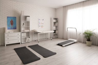 Kanepe, spor paspasları ve koşu bandı olan fizyoterapist ofisinin içi.
