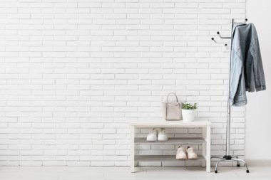 Elbise askısı ve ayakkabı standı. Koridordaki beyaz tuğla duvarın yanında çanta.