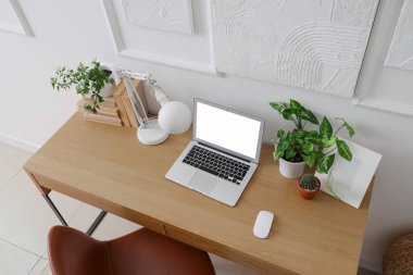 Ofiste boş dizüstü bilgisayarı ve ışık duvarı yakınında bitkileri olan bir işyeri.