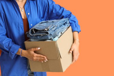 Turuncu arka planda kot pantolon ve kostüm kutusu olan genç bir kadın, yakın plan.