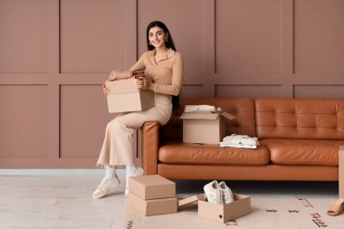 Elbise kutularıyla kanepede, kahverengi duvarın yanında oturan genç kadın.